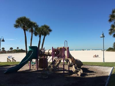 Spielplatz mit Rutschen und Klettergerüst vor blauem Himmel und weißen Sandstrand.