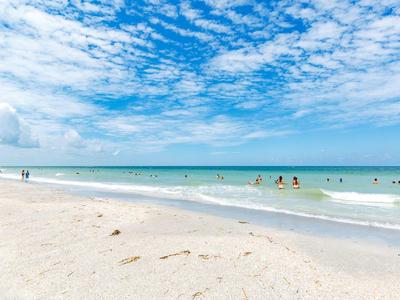 Weißer Sandstrand mit klar blauem Wasser und Menschen im flachen Meer unter blauem Himmel.