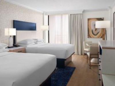 Helles Hotelzimmer mit zwei großen Betten, weißen Möbeln und Teppich auf Holzboden.