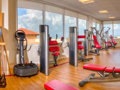 Fitnessraum mit Hantelbänken, Trainingsgeräten und großen Fenstern mit Bergblick.