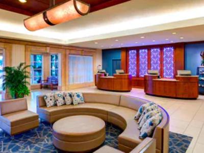 Moderne Hotellobby mit runder beiger Couch, Teppich, Pflanzen und Rezeption im Hintergrund.