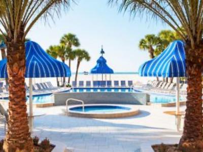 Poolbereich mit blau-weiß gestreiften Sonnenschirmen, Liegestühlen und Palmen bei sonnigem Wetter.