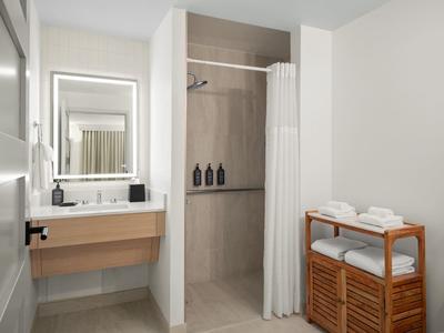 Helles modernes Badezimmer mit Holzwaschtisch, beleuchtetem Spiegel und begehbarer Dusche mit Vorhang.