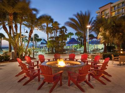 Abend am Strand mit rotem Feuerkorb, Stühlen, Palmen und Hotel im Hintergrund.