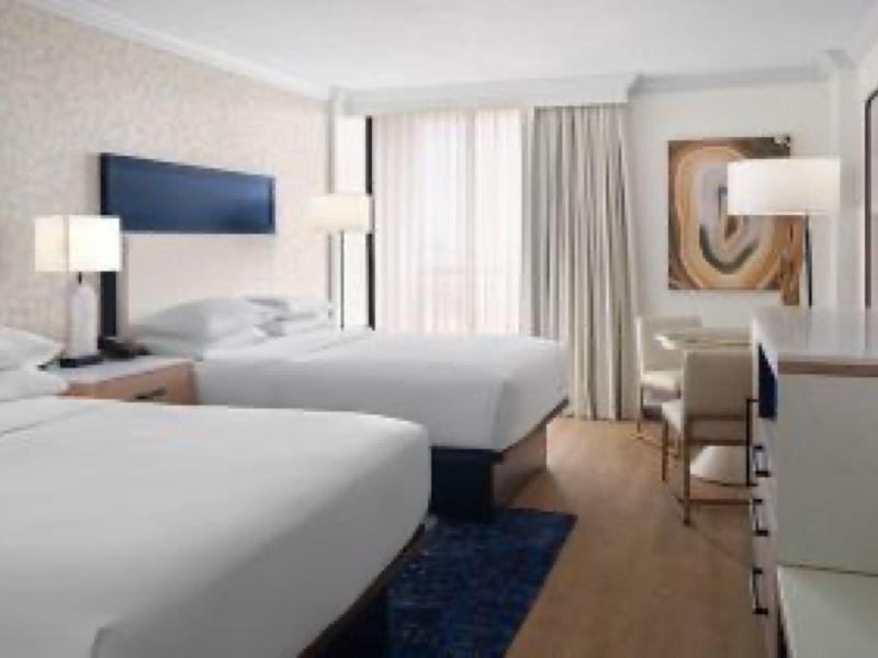 Helles Hotelzimmer mit zwei großen Betten, weißen Möbeln und Teppich auf Holzboden.