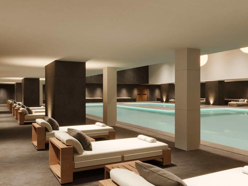 Moderní wellness s velkým krytým bazénem a lehátky s ručníky pro odpočinek.