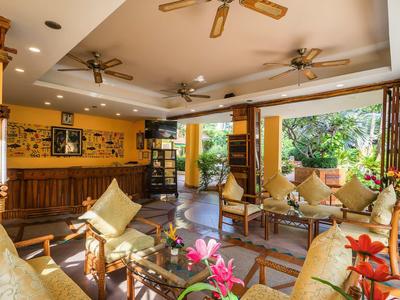 Heller Wohnraum mit Holzdekor, Deckenventilatoren, Sitzgruppen und großem Fenster mit Blick ins Grüne.