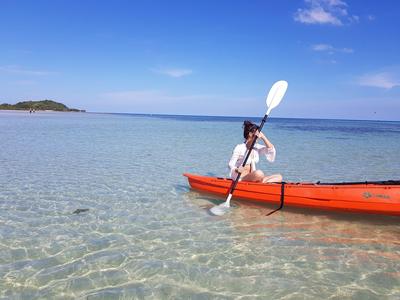 Person paddling an orange kayak in clear, shallow water under a blue sky.
