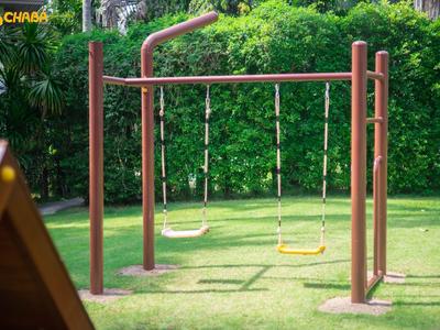 Two swings on green grass in front of dense green bushes as part of a hotel area.
