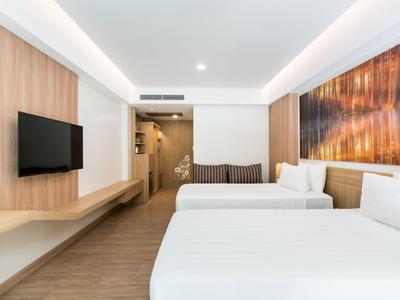 Modern hotel room with two large beds, wall-mounted TV, and cozy lighting.