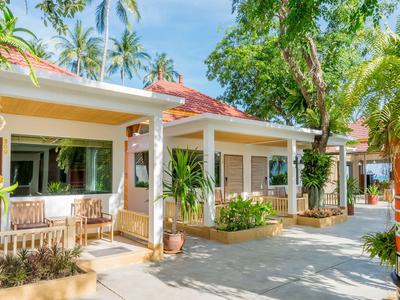 Bungalows with verandas in a tropical hotel setting with palm trees under a blue sky.