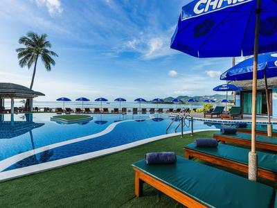 Strandresort mit Pool, blauen Sonnenschirmen, Liegen und Palmen unter blauem Himmel.