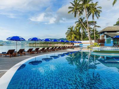 Runder Pool mit blauen Schirmen und Liegestühlen unter Palmen am Meer
