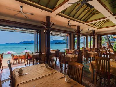 Restaurant mit Holzmöbeln und Blick auf den Strand und das Meer bei Sonnenschein.