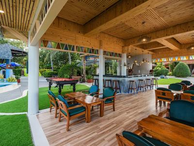 Outdoor-Lounge mit Holzdach, grünen Sesseln, Barbereich und Blick auf Pool und Garten.