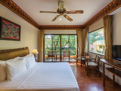 Helles Schlafzimmer mit großem Bett, Deckenventilator, Fernseher, Holzfußboden und Balkon mit Blick ins Grüne.