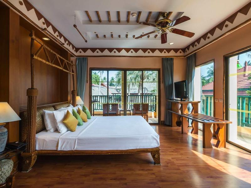 Helles Schlafzimmer mit Holzboden, großem Bett, Deckenventilator und großen Fenstern mit Gartenblick.