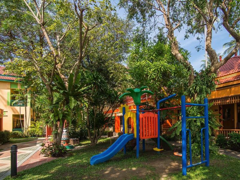 Kinderspielplatz mit bunter Rutsche und Klettergerüst, umgeben von Bäumen auf grünem Rasen.