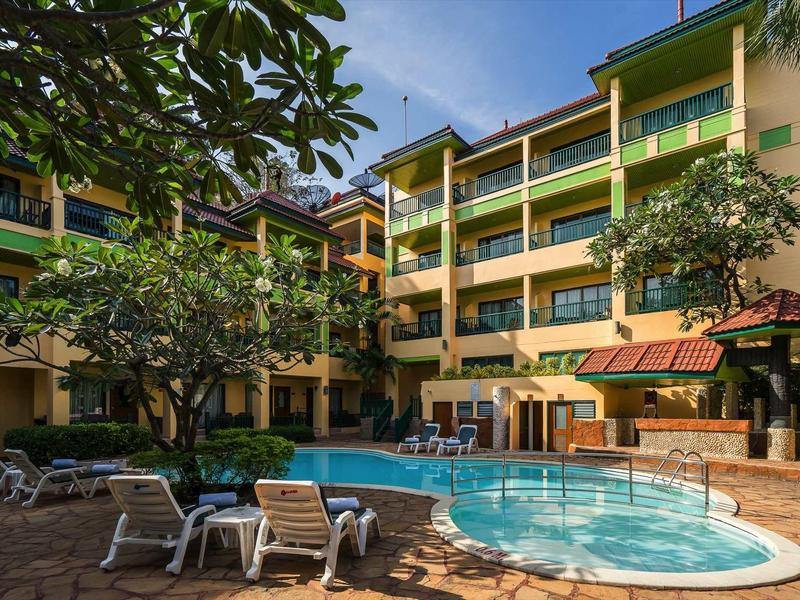 Innenhof eines Mehrfamilienhauses mit rundem Schwimmbecken, Liegestühlen und großen Bäumen.