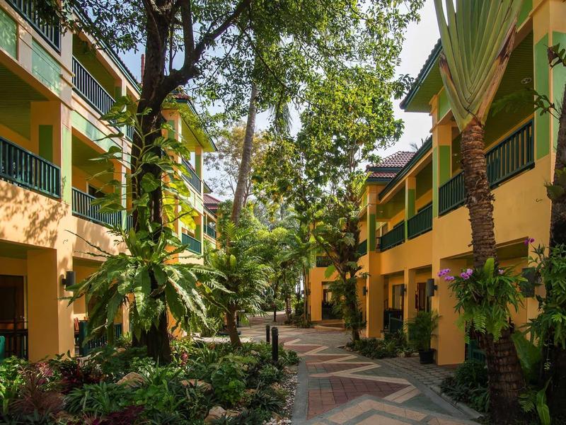 Innenhof mit orangefarbenen Gebäuden, grünen Balkonen und zahlreichen Bäumen und Pflanzen.