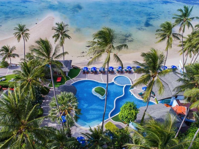 Tropischer Strand mit Palmen, Swimmingpool, Sonnenschirmen und blauer Lagune am Sandstrand.