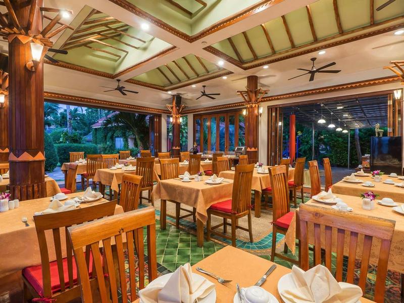 Großes Restaurant mit Holzmöbeln, gedeckten Tischen und offenem Blick auf grüne Gartenanlage.