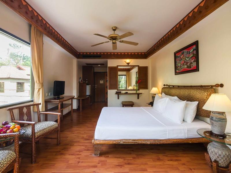 Helles Schlafzimmer mit Holzboden, großem Bett, Deckenventilator und Fenstern mit Tageslicht.