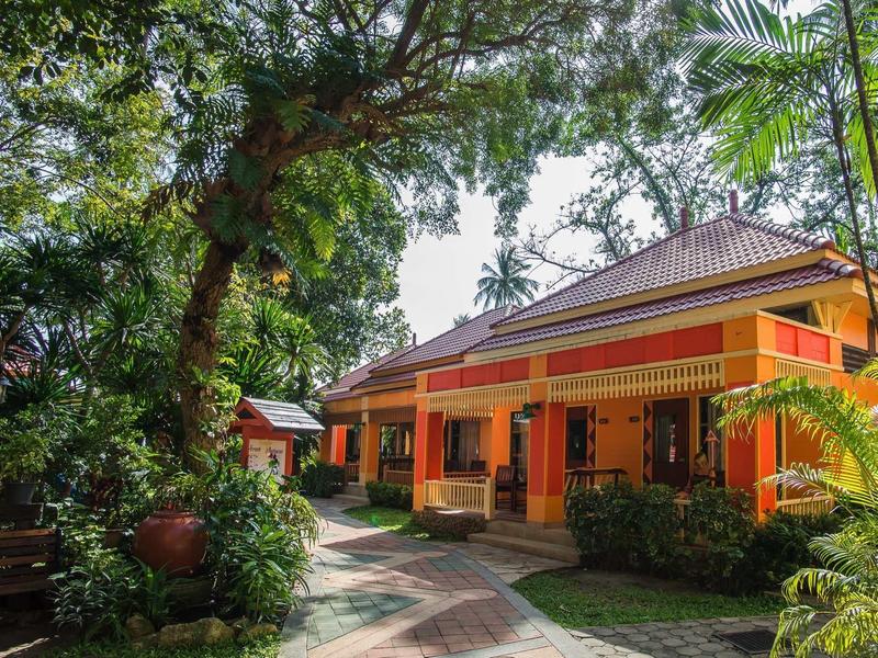 Einfarbig orange Haus in üppigem tropischem Garten mit großen Bäumen und Pflanzen.