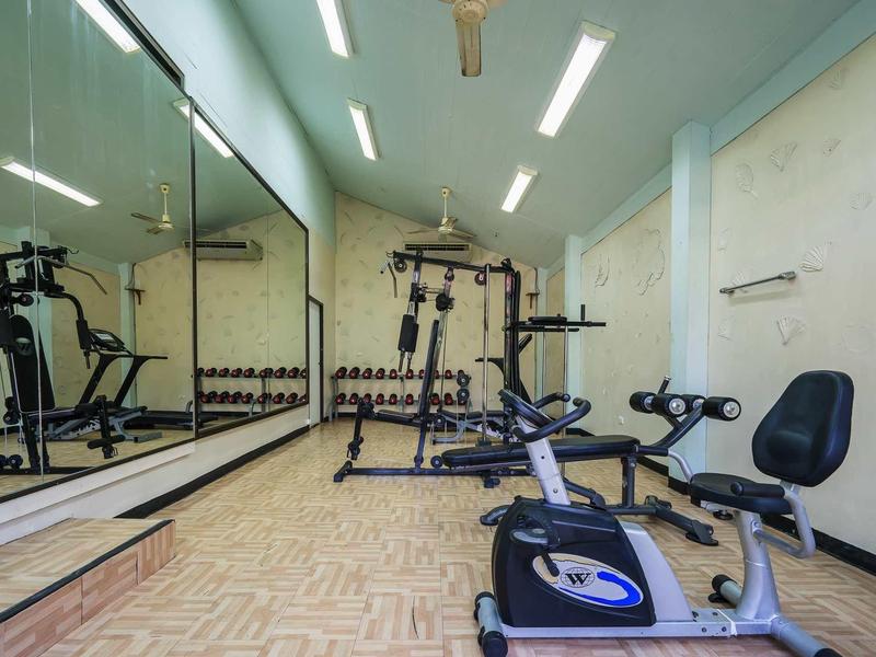 Kleiner Fitnessraum mit Fitnessgeräten, Spiegelwand, Holzfußboden und weißen Wänden.