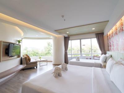 Camera d'hotel moderna con letto grande, zona salotto, TV e balcone con vista sul verde.