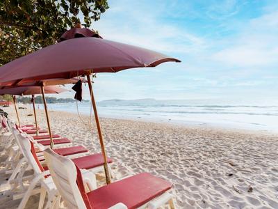 Strand mit weißen Liegestühlen und roten Sonnenschirmen an einem sonnigen Tag.