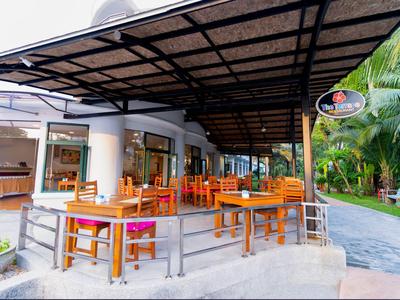 Freiluftrestaurant mit Holztischen und Stühlen unter einem überdachten Bereich neben einem tropischen Garten.