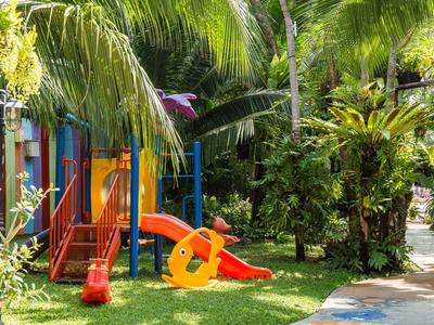 Area giochi colorata per bambini con scivolo circondata da palme e vegetazione verde su prato.