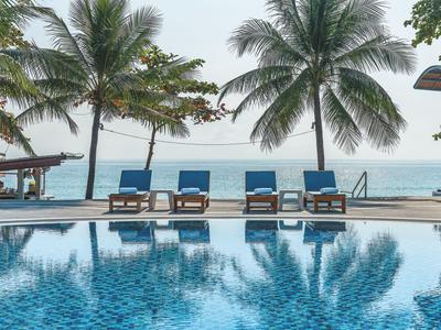 Piscina con sdraio blu e palme sulla spiaggia con vista sull'oceano.