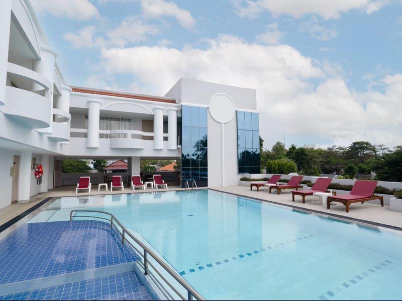 Piscina moderna dell'hotel con lettini e edificio bianco sotto il cielo azzurro.