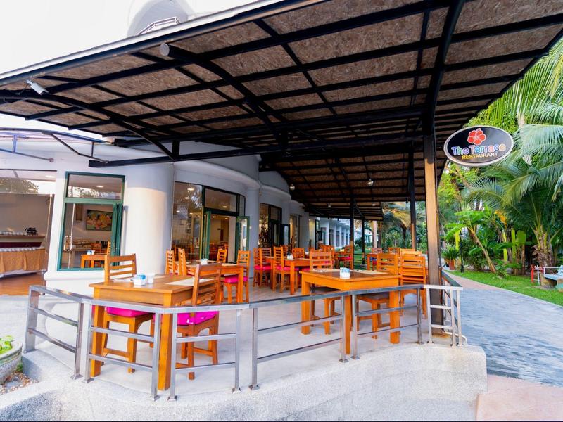 Area ristorante aperta con tavoli e sedie in legno sotto un grande tettoia accanto a una strada.