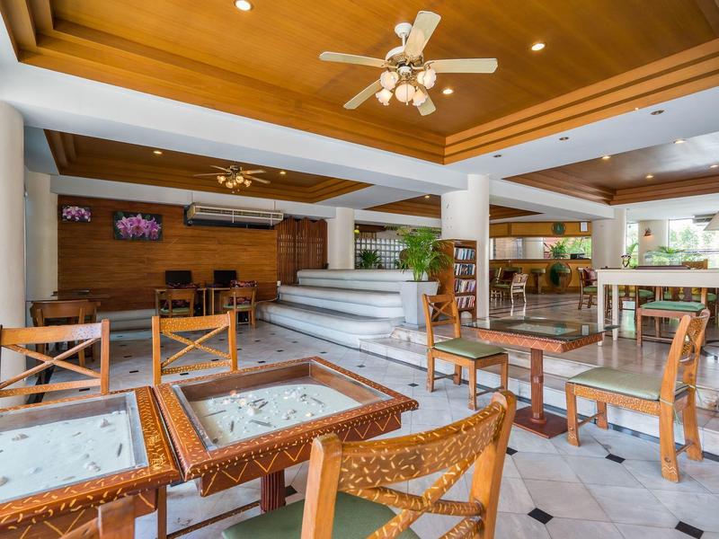 Lounge luminosa con soffitto in legno, sedie e tavoli in legno e un'area con piante sullo sfondo.