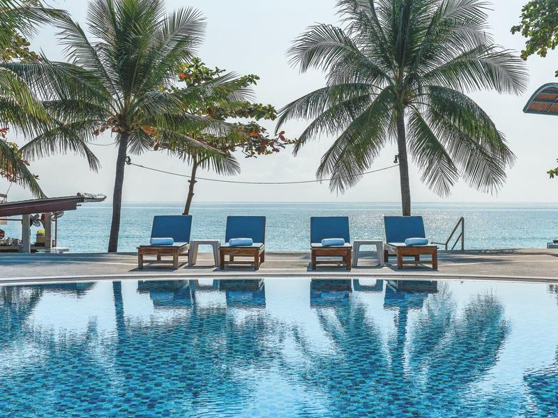 Piscina con sdraio blu e palme sulla spiaggia con vista sull'oceano.
