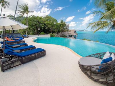 Infinity-Pool mit blauen Liegen, Palmen und Meerblick unter blau-weißem Himmel.