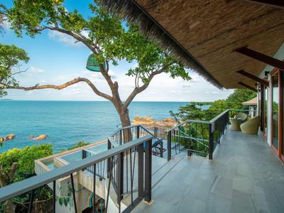 Balkon mit Fliesenboden, Holzgeländer, Blick auf Baum und blaues Meer unter klarem Himmel.
