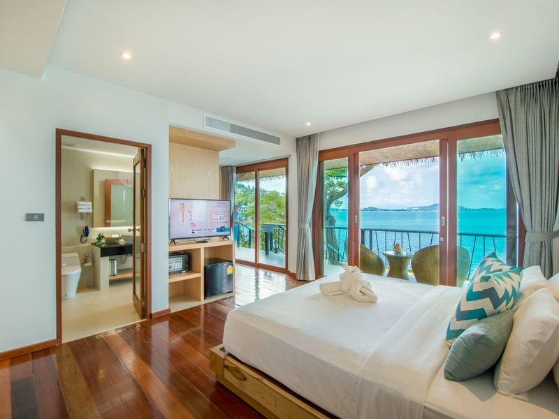 Helles Schlafzimmer mit Holzfußboden, Doppelbett, TV, und Meerblick durch große Fenster.