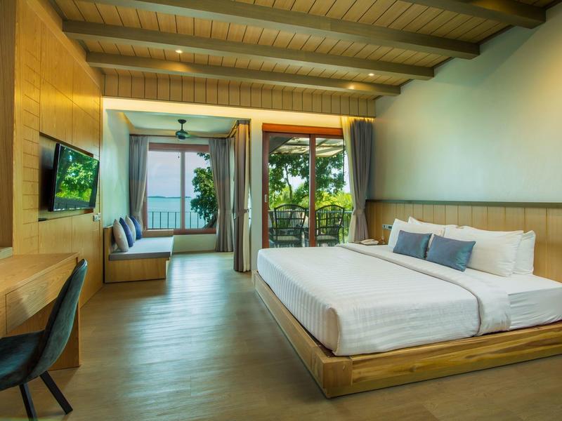 Modernes Hotelzimmer mit großem Bett, Schreibtisch, Sofa und Blick auf Terrasse mit Pflanzen.