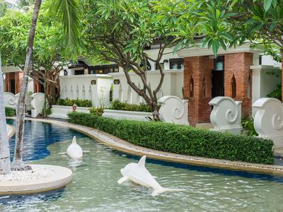 Area piscina con piante tropicali e sculture bianche decorative in un hotel.