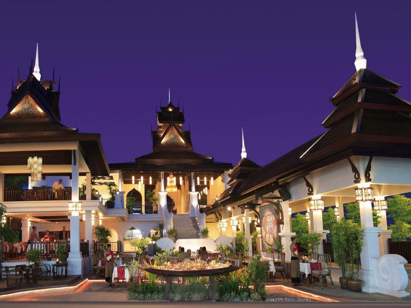 Hotel exótico iluminado con arquitectura asiática por la noche, rodeado de jardines y fuentes.