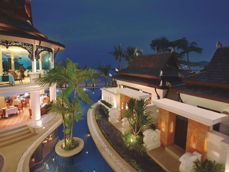 Lujoso complejo hotelero de noche con piscina iluminada y vegetación tropical.