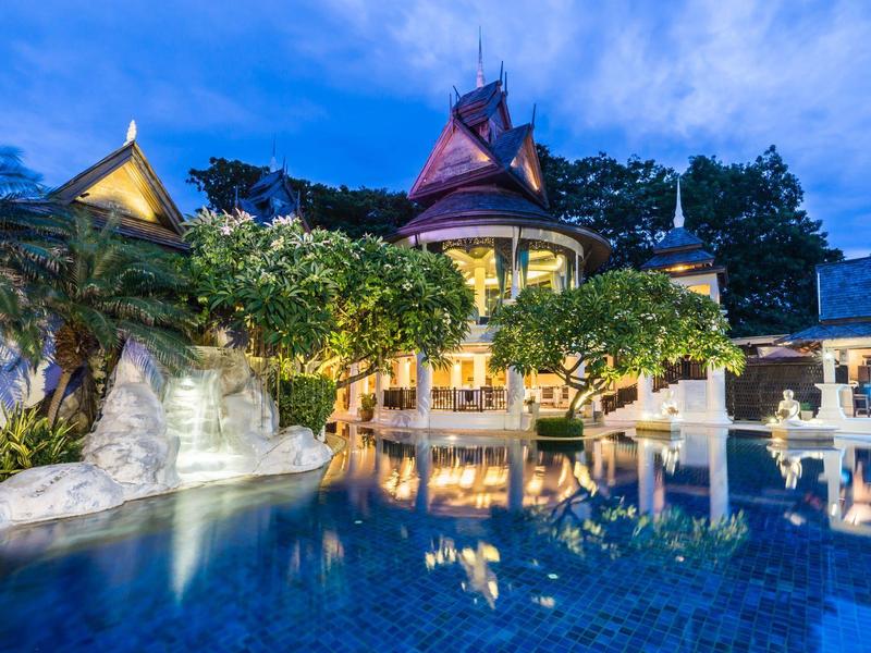 Resort de lujo con piscina iluminada y pabellones rodeados de árboles al atardecer.