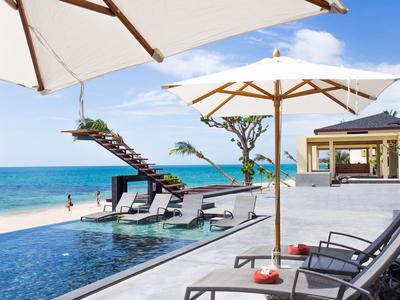 Luxuriöse Hotelpoolanlage mit Strandblick, Liegen und großen Sonnenschirmen an der Küste.