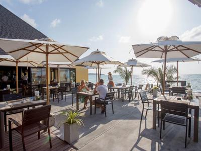 Offenes Restaurant mit Tischen, Stühlen und Sonnenschirmen an sonnigem Meerblick.