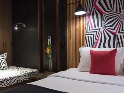 Camera d'hotel moderna con motivo geometrico sulla parete e letto rosso e bianco.