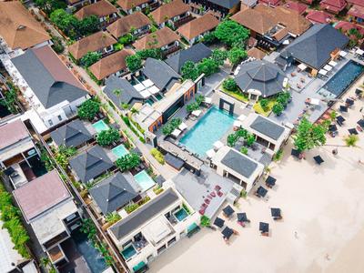 Veduta aerea di un resort sulla spiaggia con piscine, lettini e case residenziali vicine.